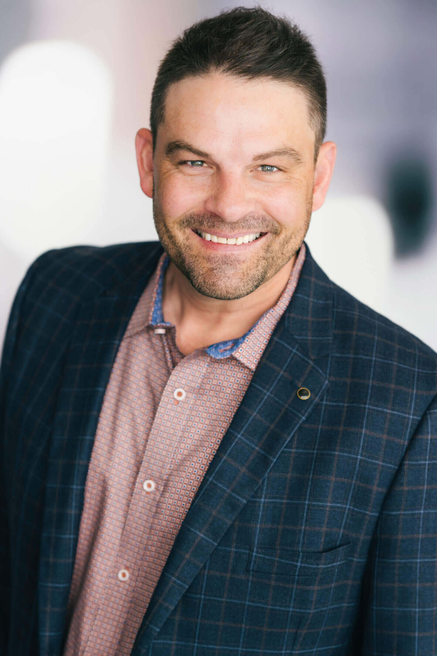 Smiling man in a checkered blazer and collared shirt.