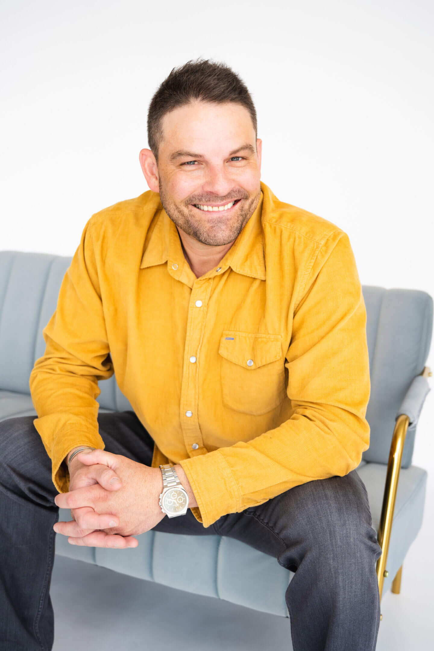 Smiling man in a yellow shirt sitting on a chair.