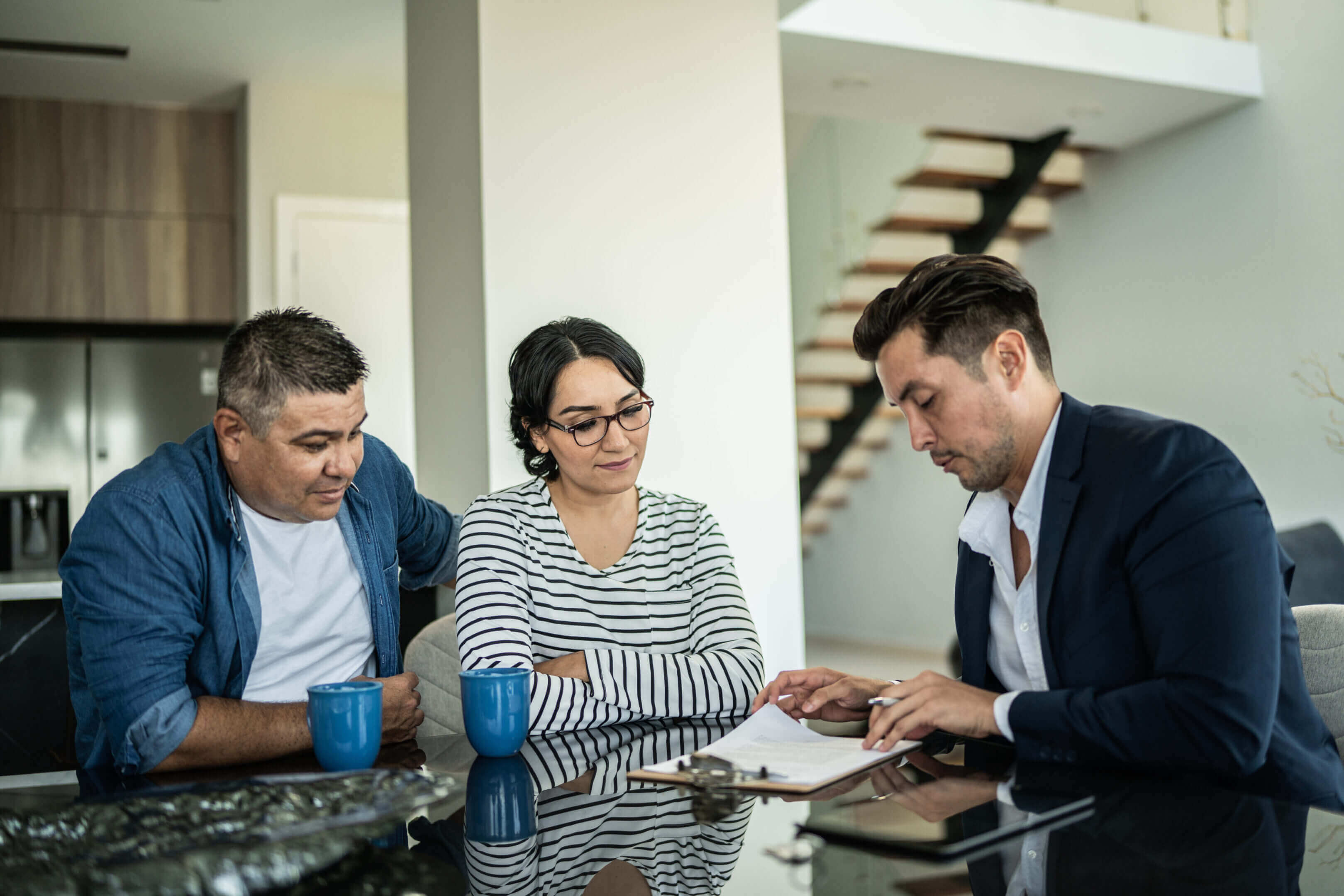 Three people discussing documents at a table in a modern office.