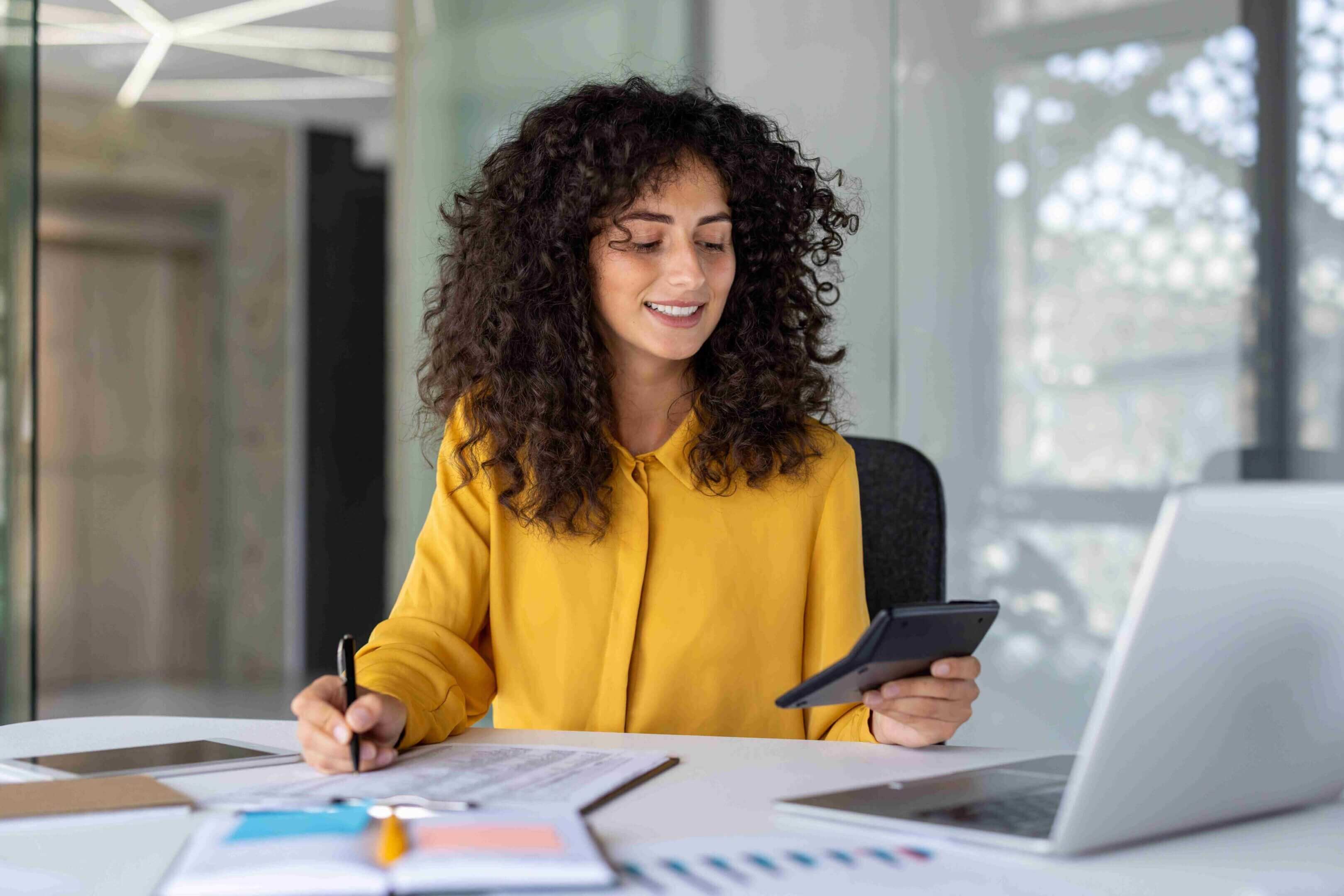 A woman in a yellow blouse using a smartphone at her desk.