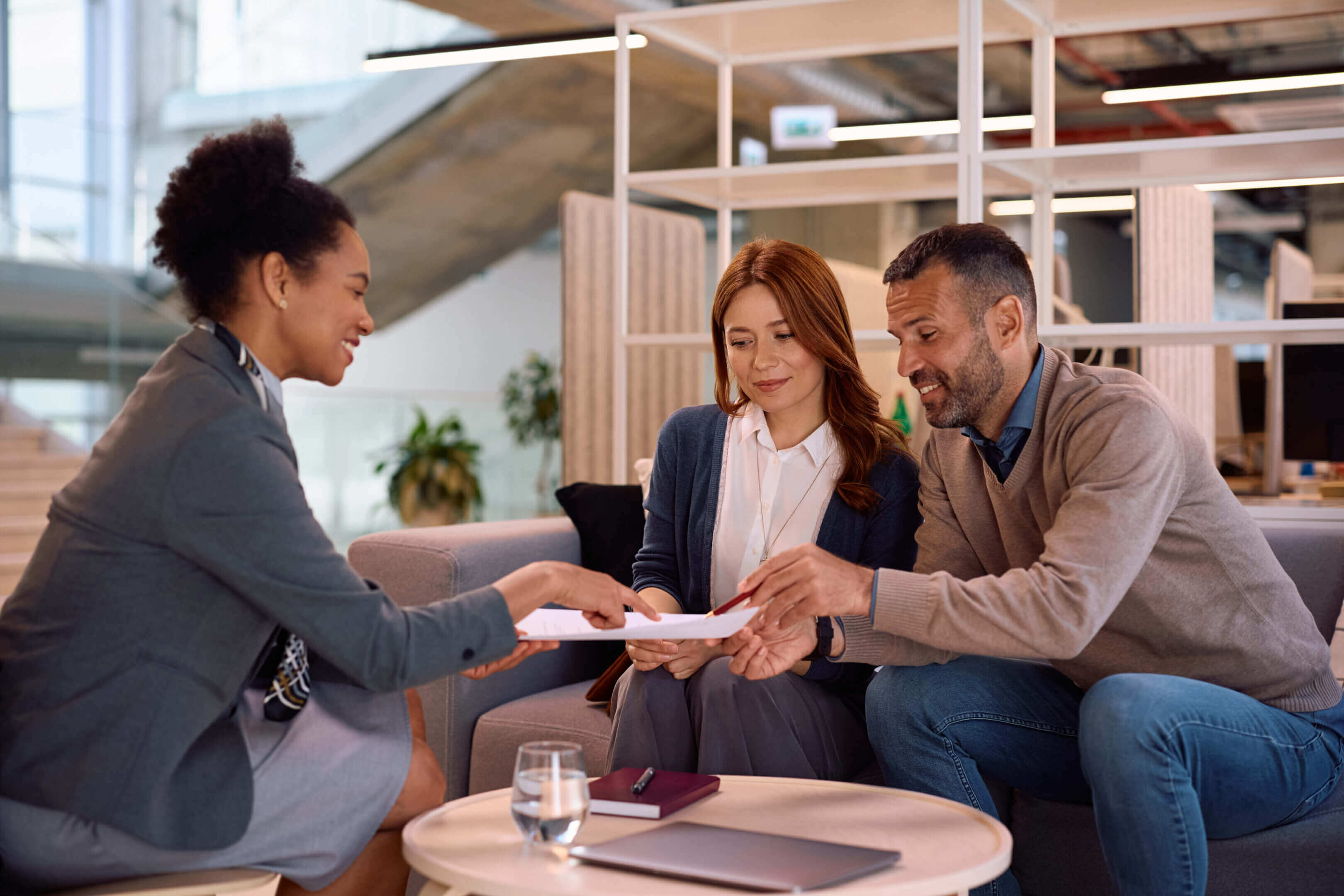 Couple signing documents with a consultant in a modern office.