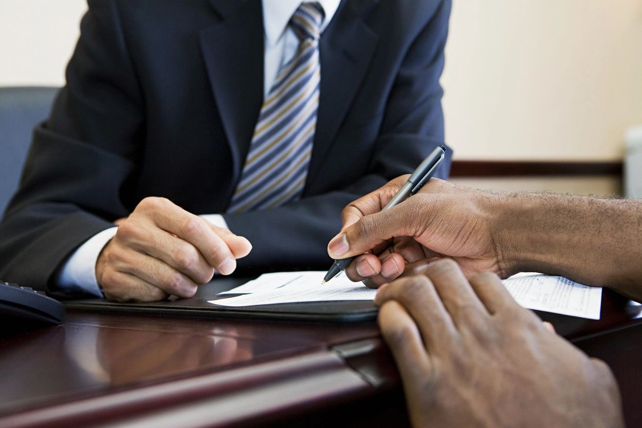 Two professionals signing documents at a formal meeting.