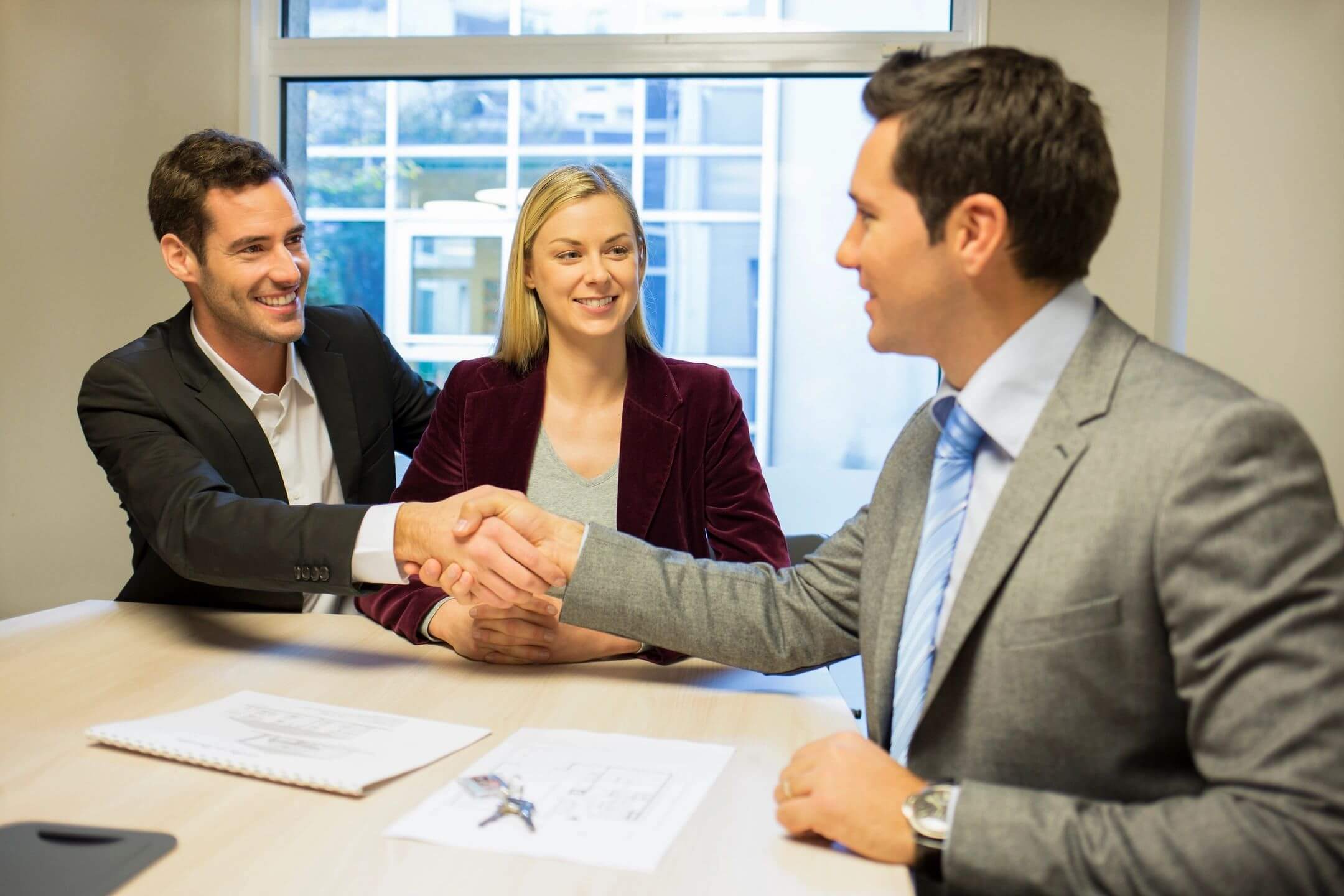 Two men shaking hands during a business meeting with a smiling woman present.