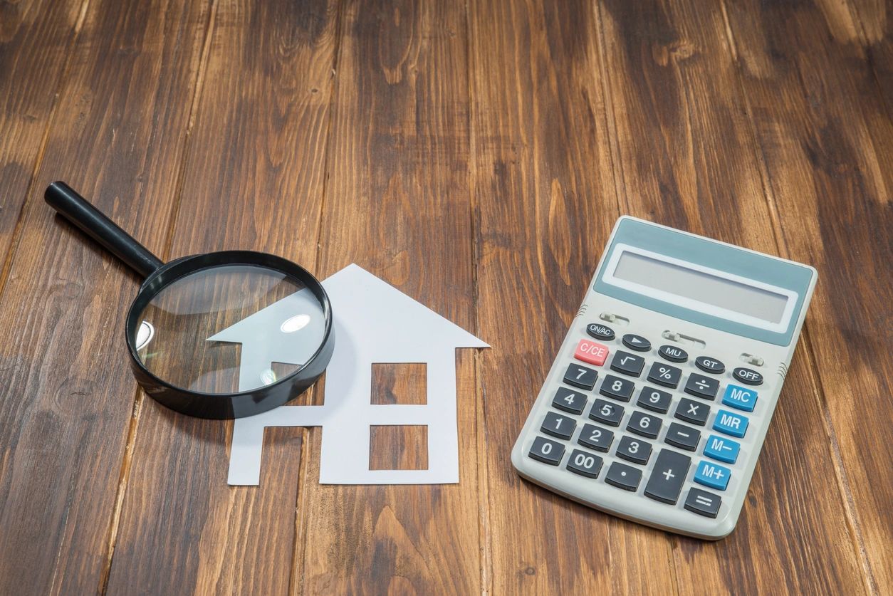 House model, magnifying glass, and calculator on wooden table.