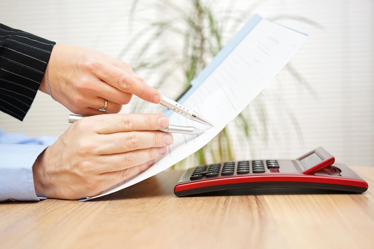 Person reviewing documents with a pen and calculator nearby.