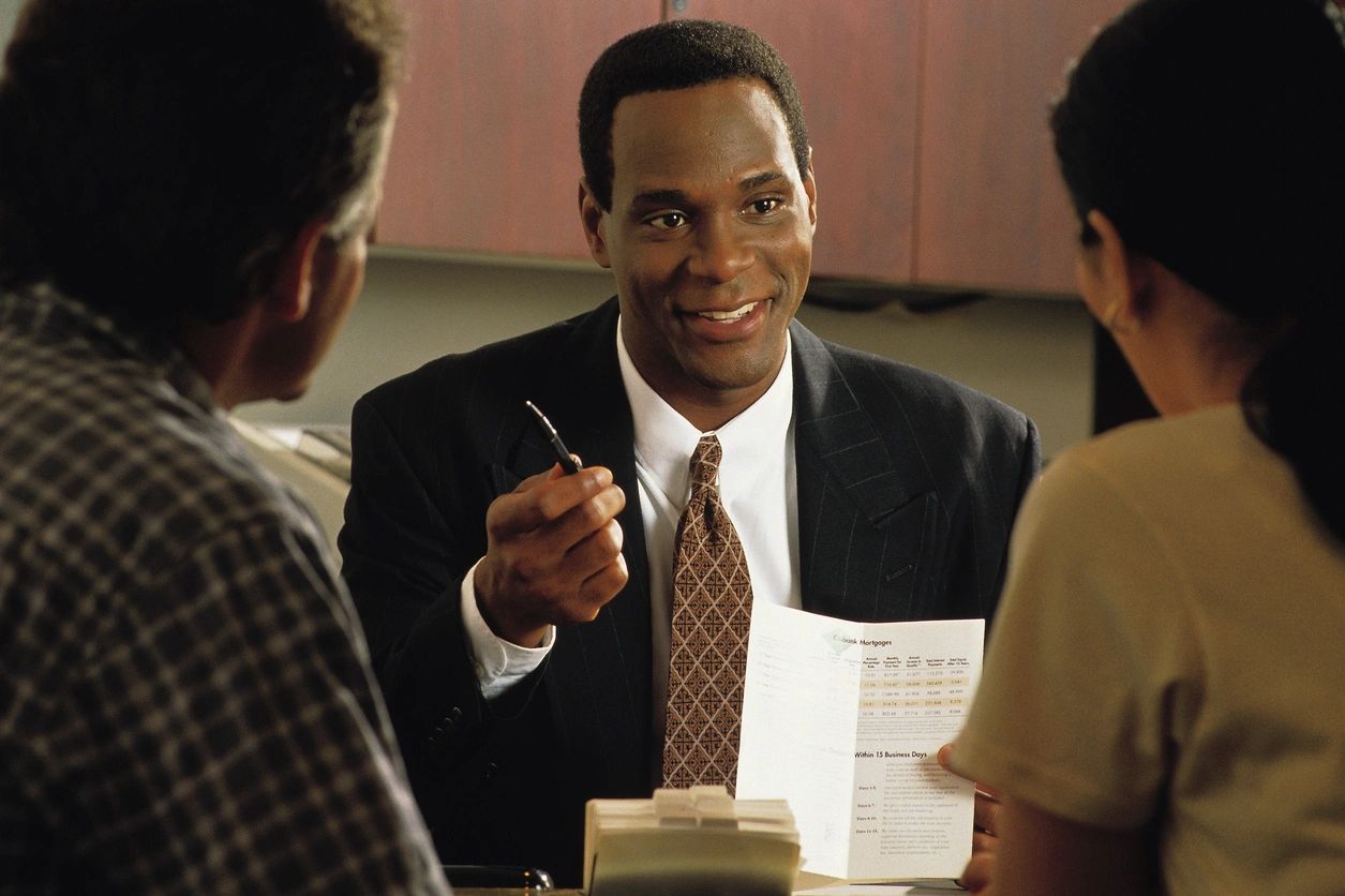 A man in a suit holding papers and a pen, smiling during a meeting.